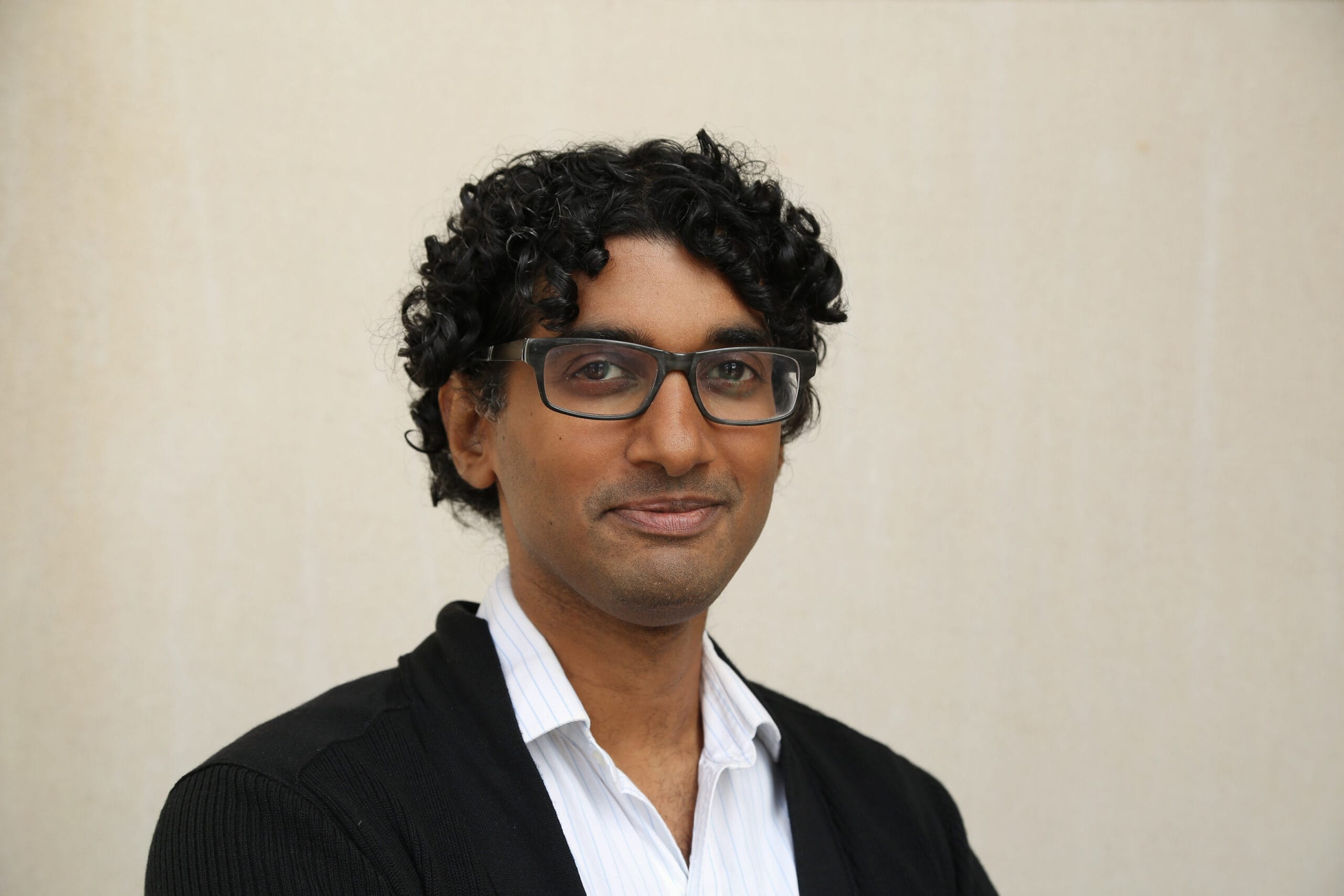 Suresh Naisu smiles against a beige wall
