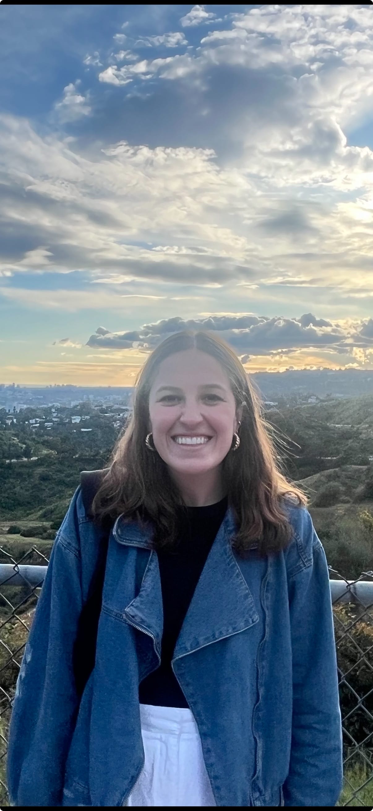 A headshot of AnneMarrie smiling with the sky and greenery in the background